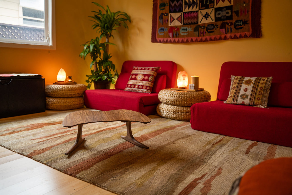 Warm, calming meditation room with floor seating, cushions, salt lamps, and a handcrafted HoM walnut piece — a comfortable, low-to-the-ground setting for seated meditation.